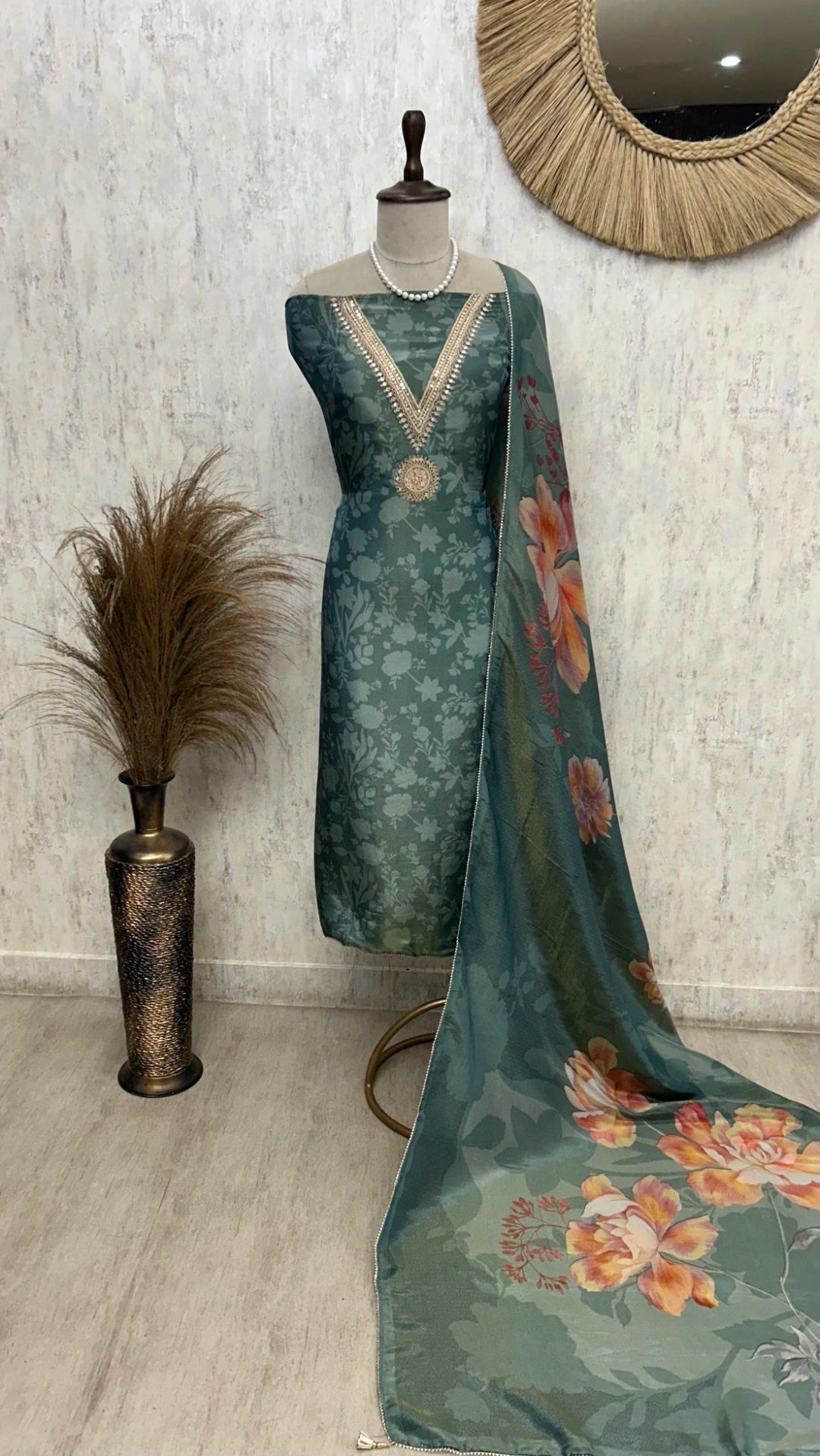 Teal traditional outfit with floral dupatta on a mannequin against a textured wall.