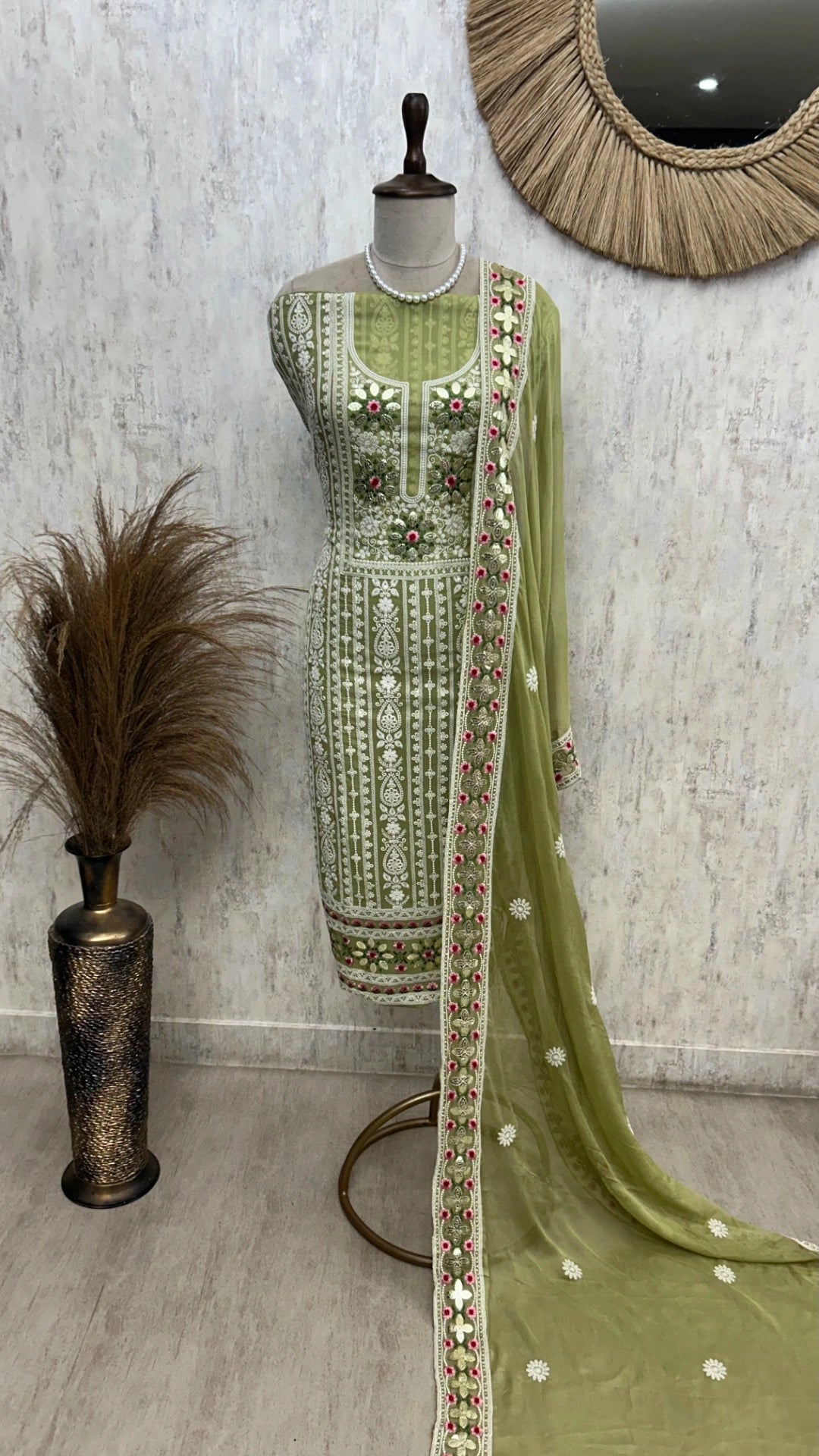 Green embroidered traditional outfit on a mannequin against a textured wall.